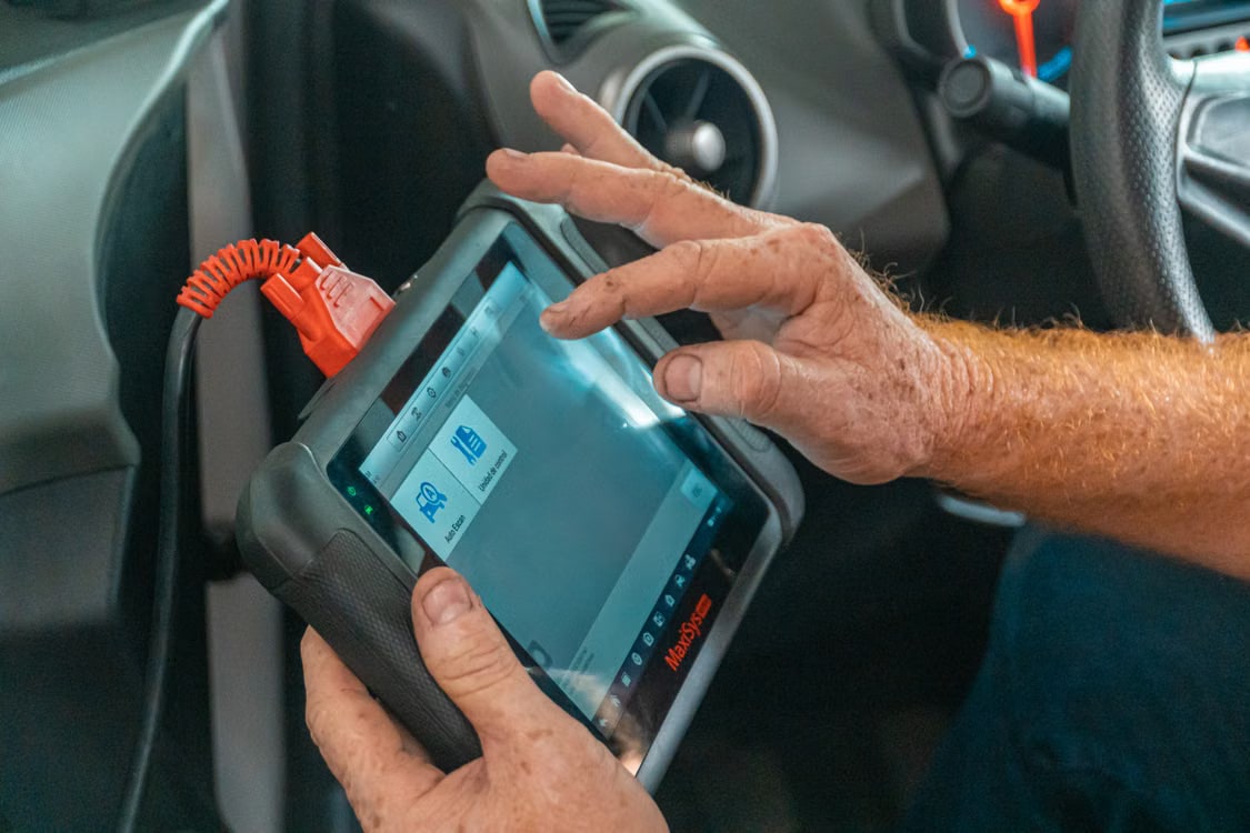 A technician using a real automotive diagnostic scan tool inside a vehicle